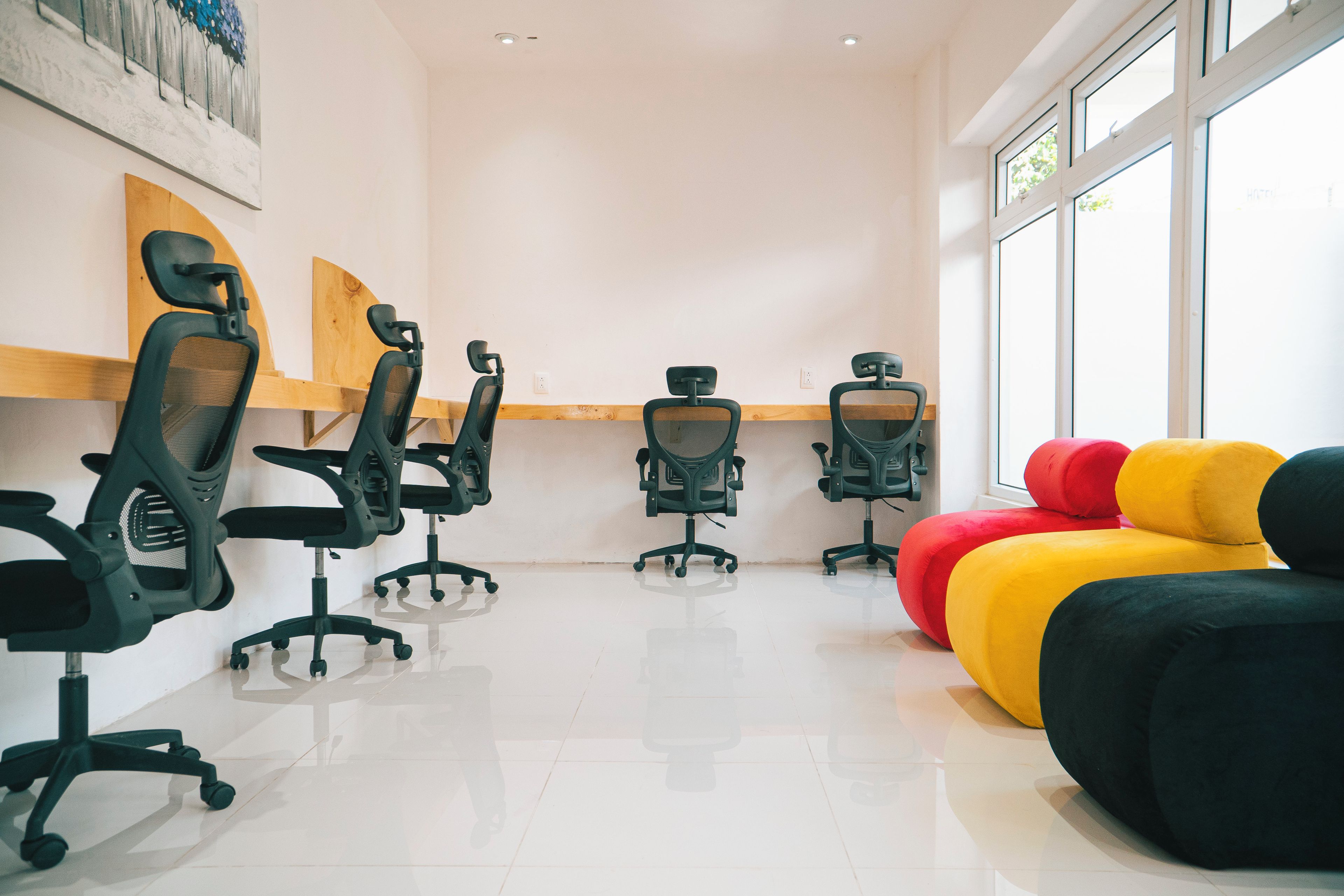 Un espace de bureau moderne doté de chaises ergonomiques, d’une grande fenêtre et d’un coin détente avec des fauteuils en forme de sac de haricots aux couleurs vives.