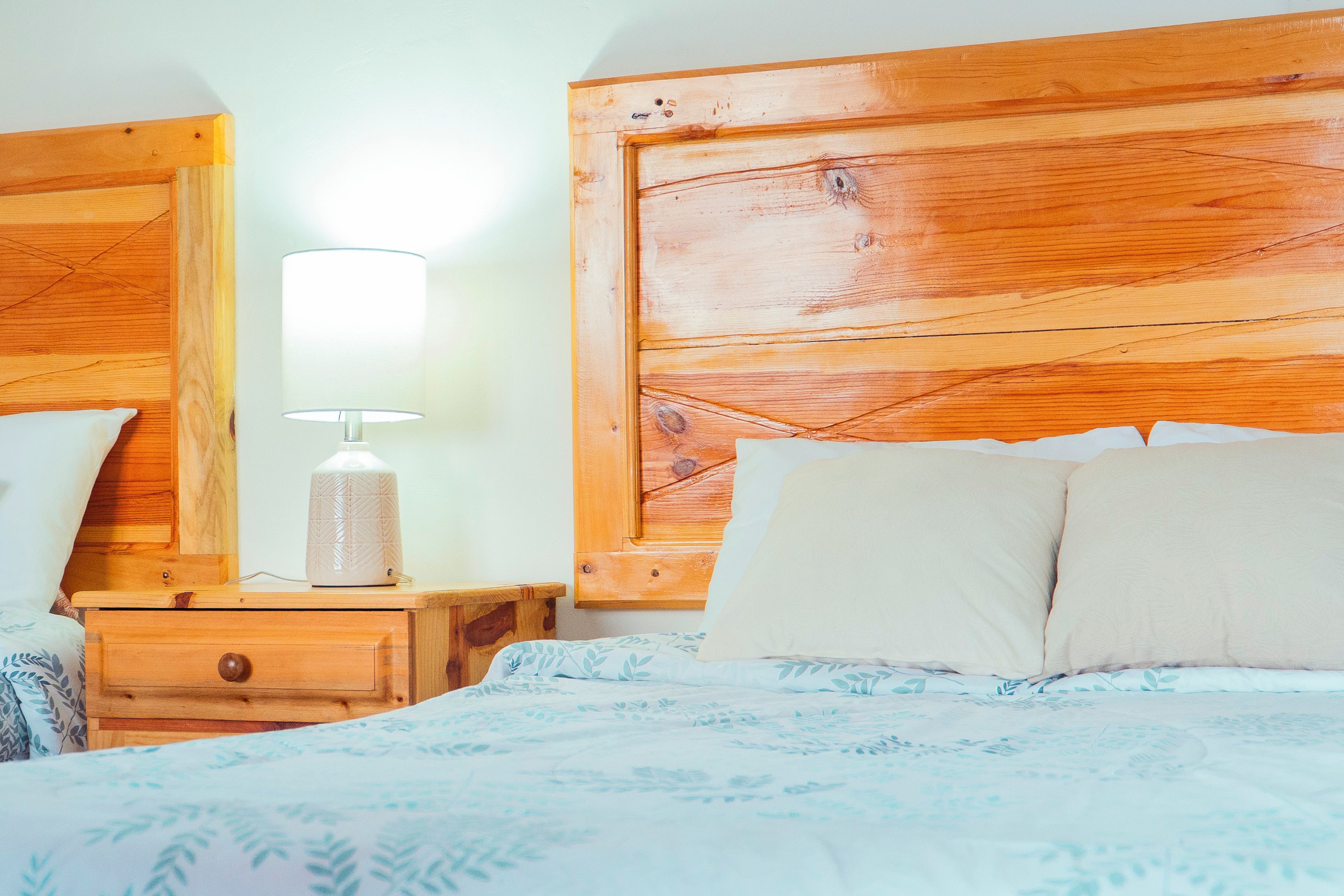 Un dormitorio con cabecera de madera, una mesita de noche con lámpara y una cama con colcha estampada.