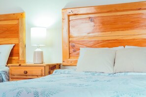 Un dormitorio con cabecera de madera, una mesita de noche con lámpara y una cama con colcha estampada.