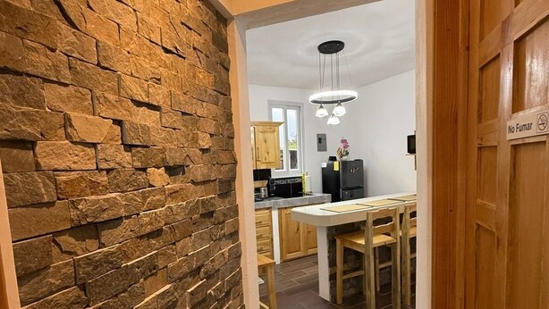 Un couloir avec un mur en pierre, une porte en bois et une vue sur un coin cuisine comprenant une table et des chaises.