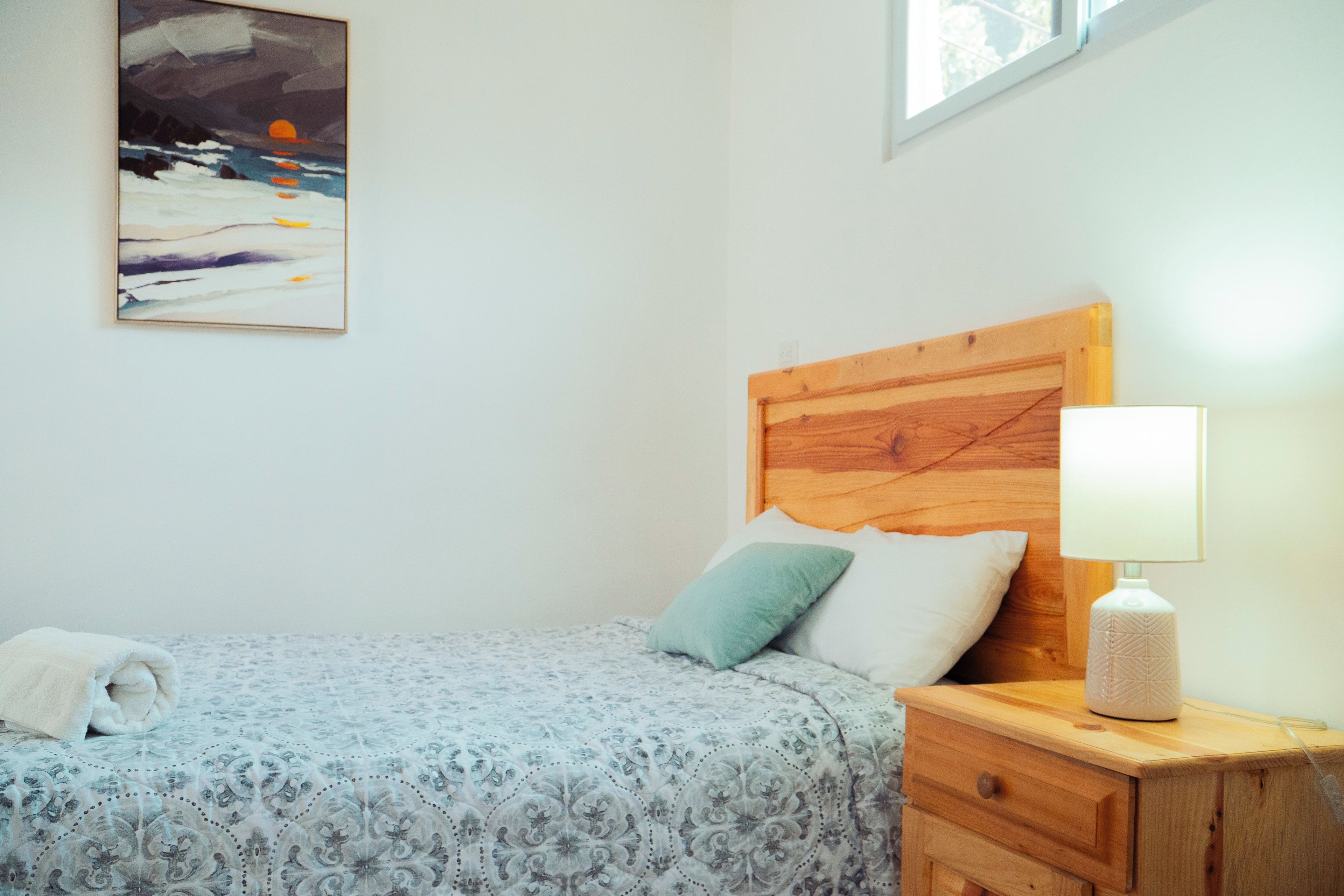Une chambre à coucher avec un lit, des oreillers, une table de chevet avec une lampe et un tableau accroché au mur.