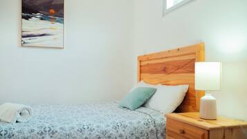 Une chambre à coucher avec un lit, des oreillers, une table de chevet avec une lampe et un tableau accroché au mur.