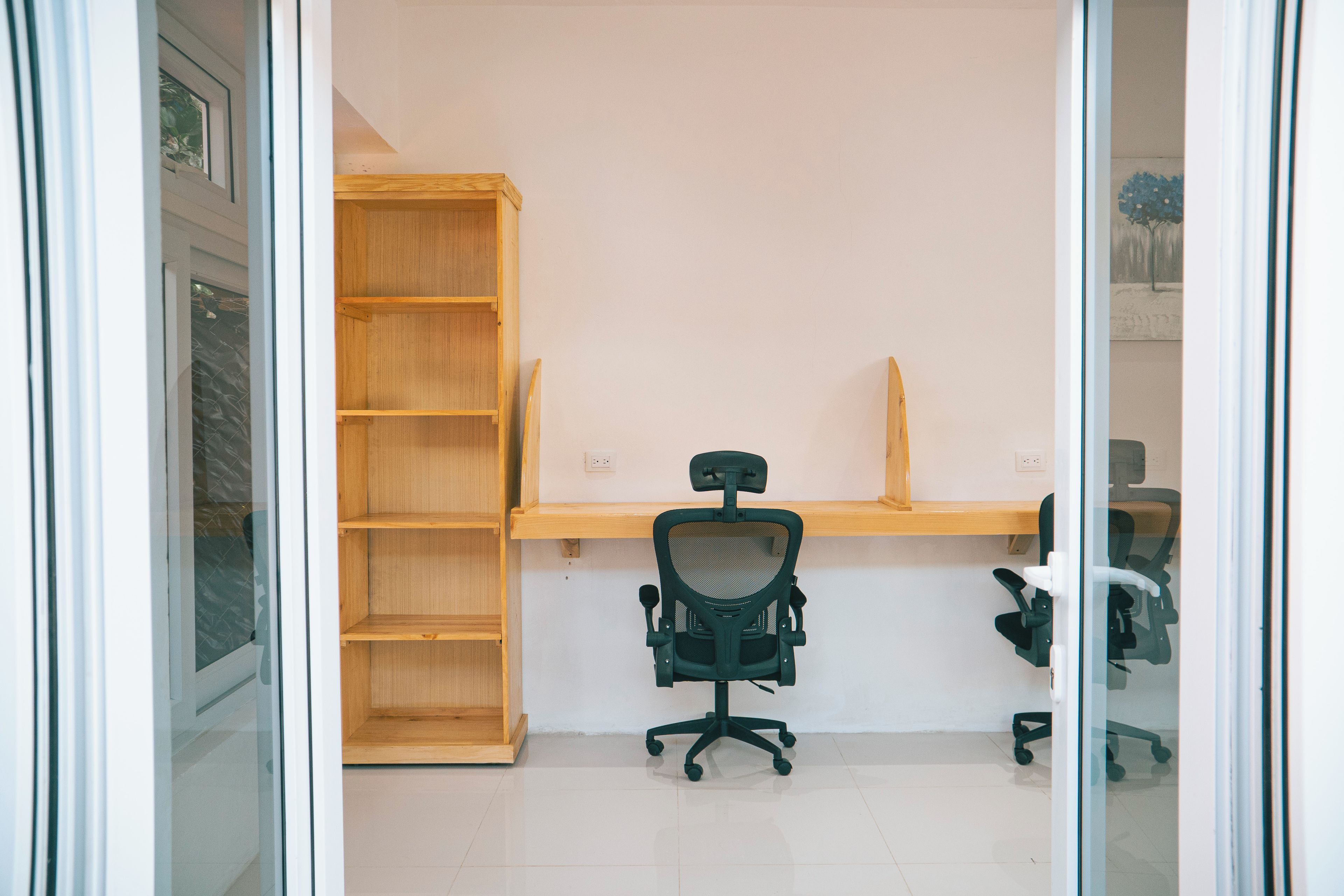 Een kamer met een houten bureau, een zwarte bureaustoel en een open kast.