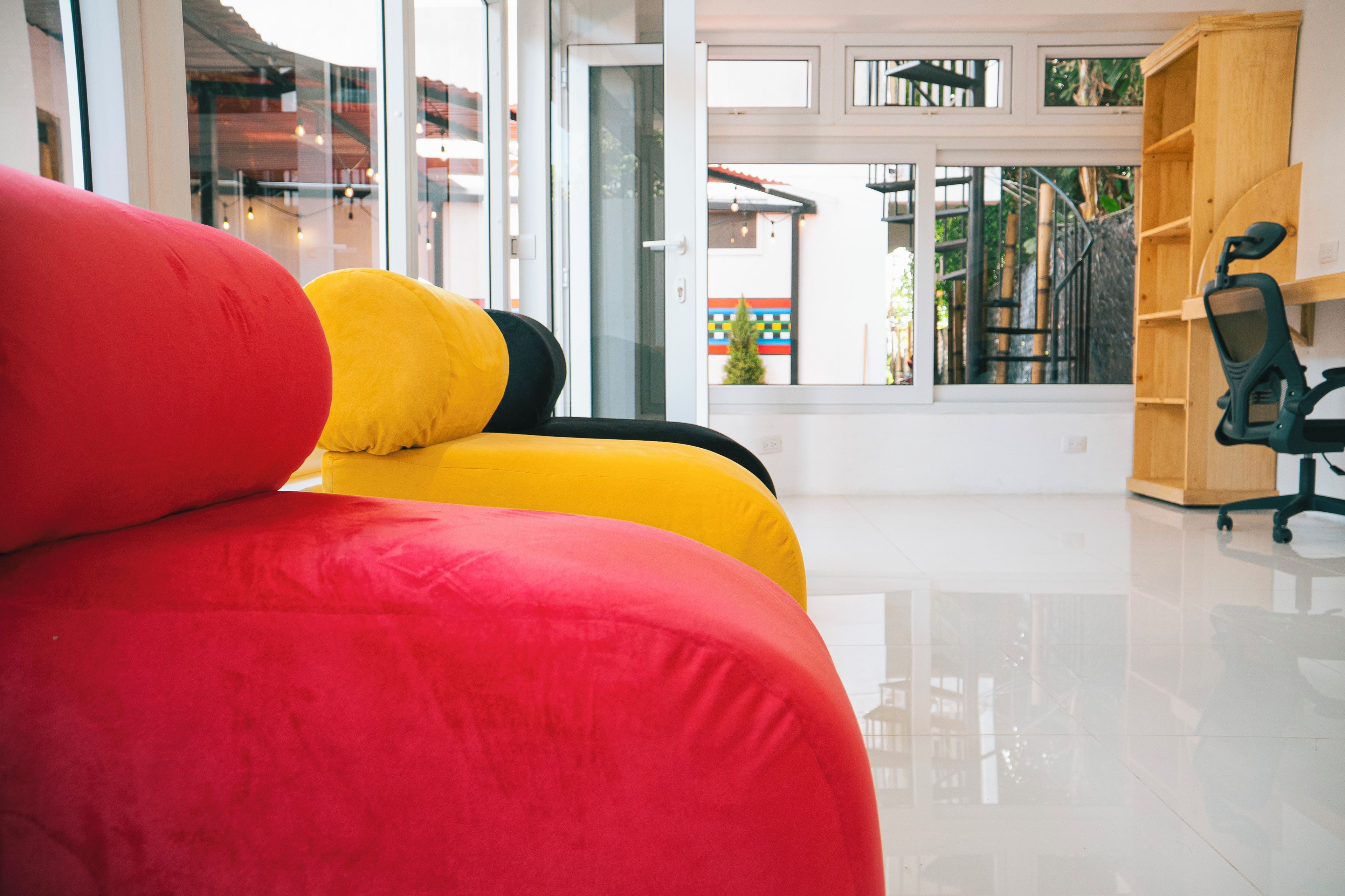 Ein modernes Interieur mit einem roten und gelben Sofa, einem schwarzen Bürostuhl und einem Holzregal.