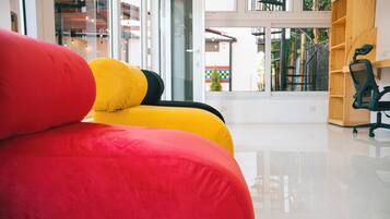 Ein modernes Interieur mit einem roten und gelben Sofa, einem schwarzen Bürostuhl und einem Holzregal.