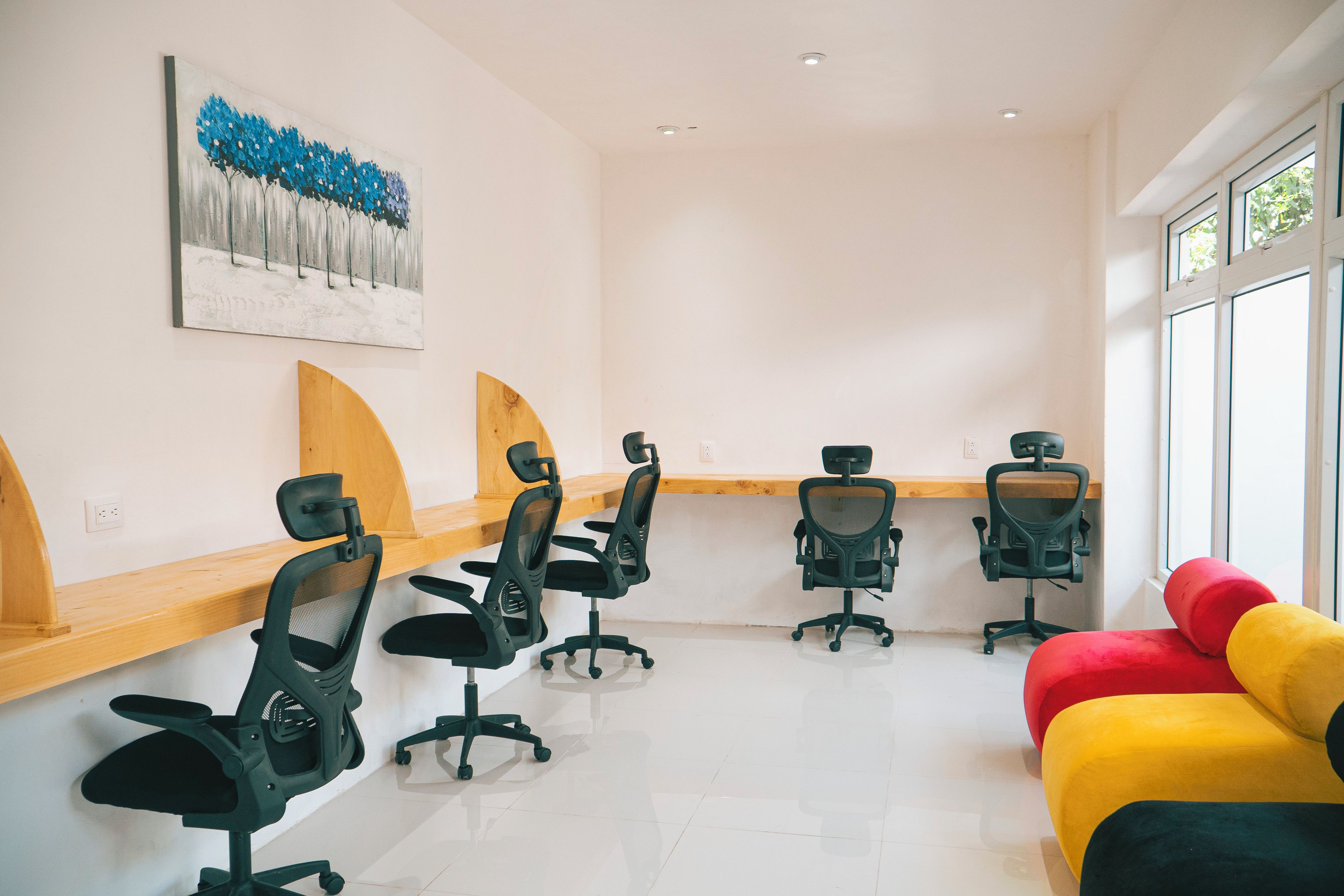 A conference room with four black office chairs, a wooden desk, a colorful couch, and a painting on the wall.