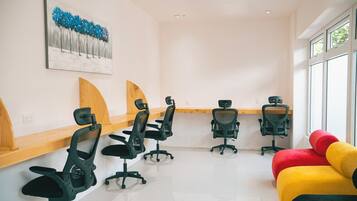 A conference room with four black office chairs, a wooden desk, a colorful couch, and a painting on the wall.