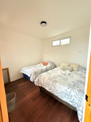Quarto com duas camas, uma janela, uma luminária no teto e uma lixeira.