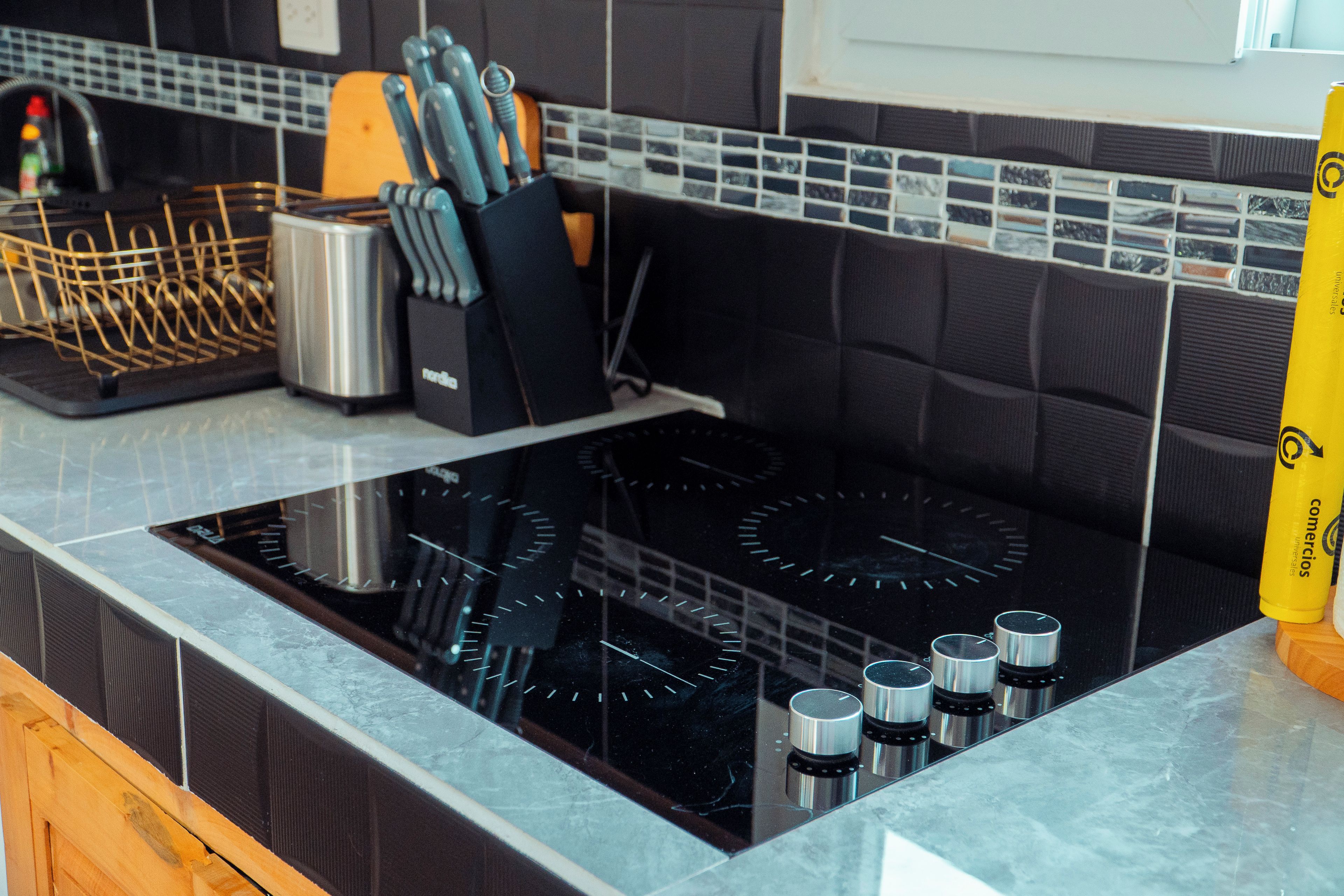 Una cucina con un piano cottura nero, un portachiodi e un contenitore giallo.