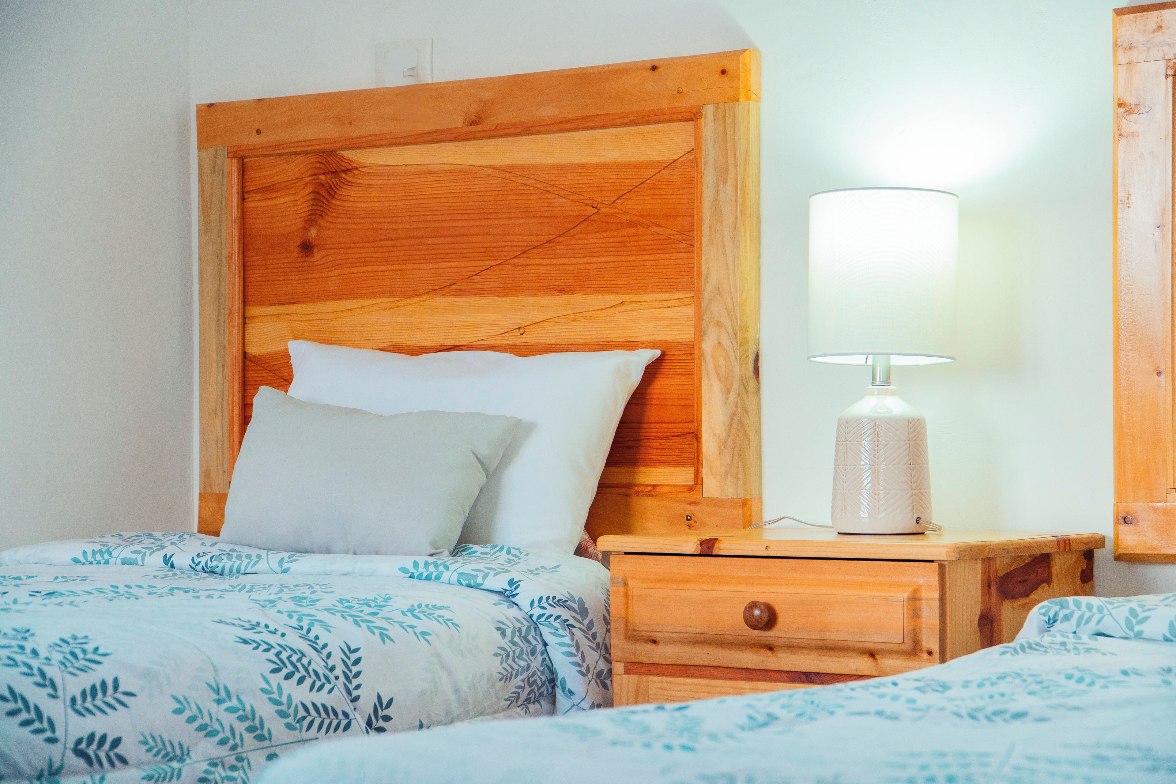 A wooden headboard with a nightstand and a lamp. There are two beds with patterned bedding.