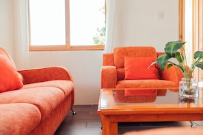 Una habitación con un sofá y una silla, ambos de color naranja intenso, una pequeña mesa y una planta en maceta sobre la mesa.