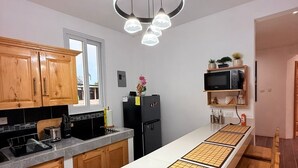 Une cuisine moderne avec des meubles en bois, un plan de travail blanc, un réfrigérateur noir et un luminaire suspendu.