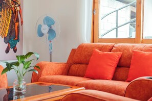 Ein Zimmer mit einer Couch, einem Ventilator, einem Fenster und einer Pflanze.