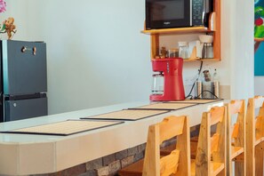 Una cocina con microondas, cafetera y sillas de madera.