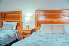 Ett hotellrum med två sängar i trä, ett nattduksbord med en lampa och ett vägguttag.
