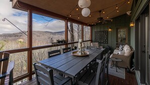 A covered outdoor dining area with a table and chairs, string lights, and a view of the surrounding landscape.