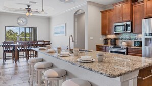 Una cocina moderna con encimeras de granito, electrodomésticos de acero inoxidable, armarios de madera y una isla central con taburetes de bar.