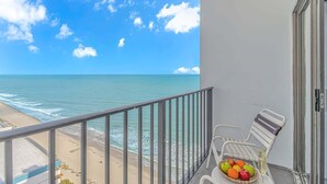 Ein Balkon mit Blick auf den Ozean, einen Strand und einem Tisch mit Früchten und einem Glas Champagner.