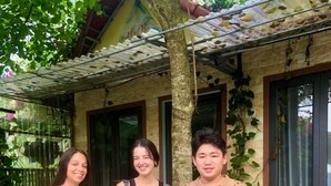 Three people standing in front of a building with a tiled roof and a tree. - Homestay An Huy Mai Châu (Mai Chau)