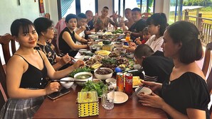 A group of people seated around a table with various dishes, drinks, and a small yellow basket. - Homestay An Huy Mai Châu (Mai Chau)