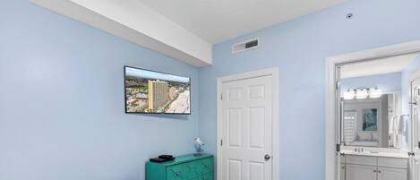 A bedroom with a bed, a teal dresser, a white door, and a bathroom visible through an open door.