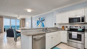 A modern kitchen with a dishwasher, microwave, and oven, a dining area with a view, and a large abstract painting on the wall. - "Emerald Isle" | Beachfront | Amazing beach views | Heated Community Pool | Fitness center (Panama City Beach)