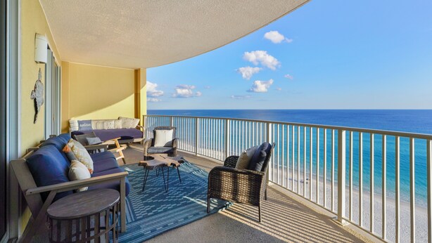 A balcony with a sofa, chairs, and a small table, overlooking a beach. - "Emerald Isle" | Beachfront | Amazing beach views | Heated Community Pool | Fitness center (Panama City Beach)