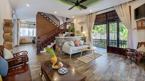 A spacious living area with a wooden staircase, a sofa set, a coffee table, and a dining table with fruit.