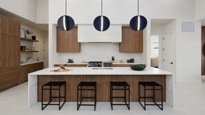 A modern kitchen with a central island, pendant lights, and wooden cabinetry. - Luna Luxe - Pool Heat Avail- Hot Tub - Fire Pit! (Scottsdale)