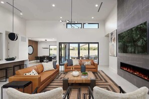 A spacious living area with a fireplace, a dining table, and a large window overlooking a garden. - Luna Luxe - Pool Heat Avail- Hot Tub - Fire Pit! (Scottsdale)