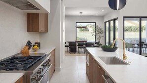 A modern kitchen with a gas stove, wooden cabinets, and a large window overlooking a patio area. - Luna Luxe - Pool Heat Avail- Hot Tub - Fire Pit! (Scottsdale)