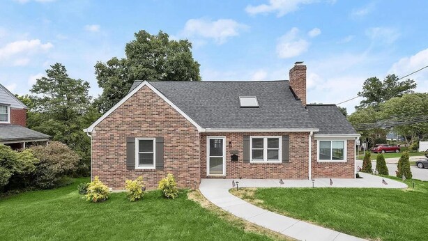 A single-story brick house with a gabled roof, a front porch, and a small front yard with trimmed bushes. - Cozy 1-bedroom apartment with king size bed. (Towson)