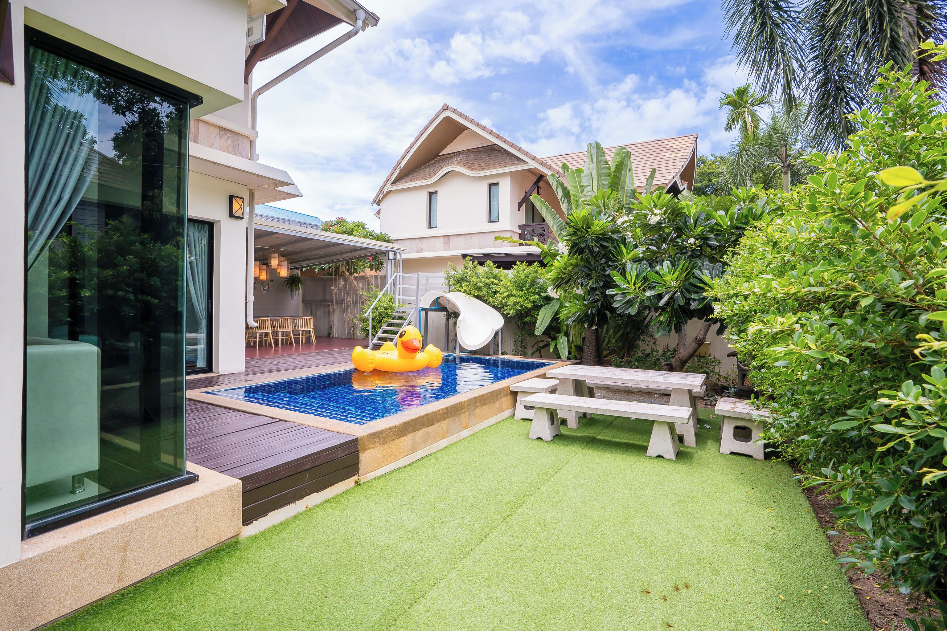 Une maison moderne dotée d’une piscine, d’un toboggan et d’un espace patio avec une table et des chaises.