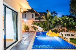 A swimming pool with a slide, surrounded by tropical plants and a yellow duck float. - Natcha Pool Villa by Warin (Pattaya)