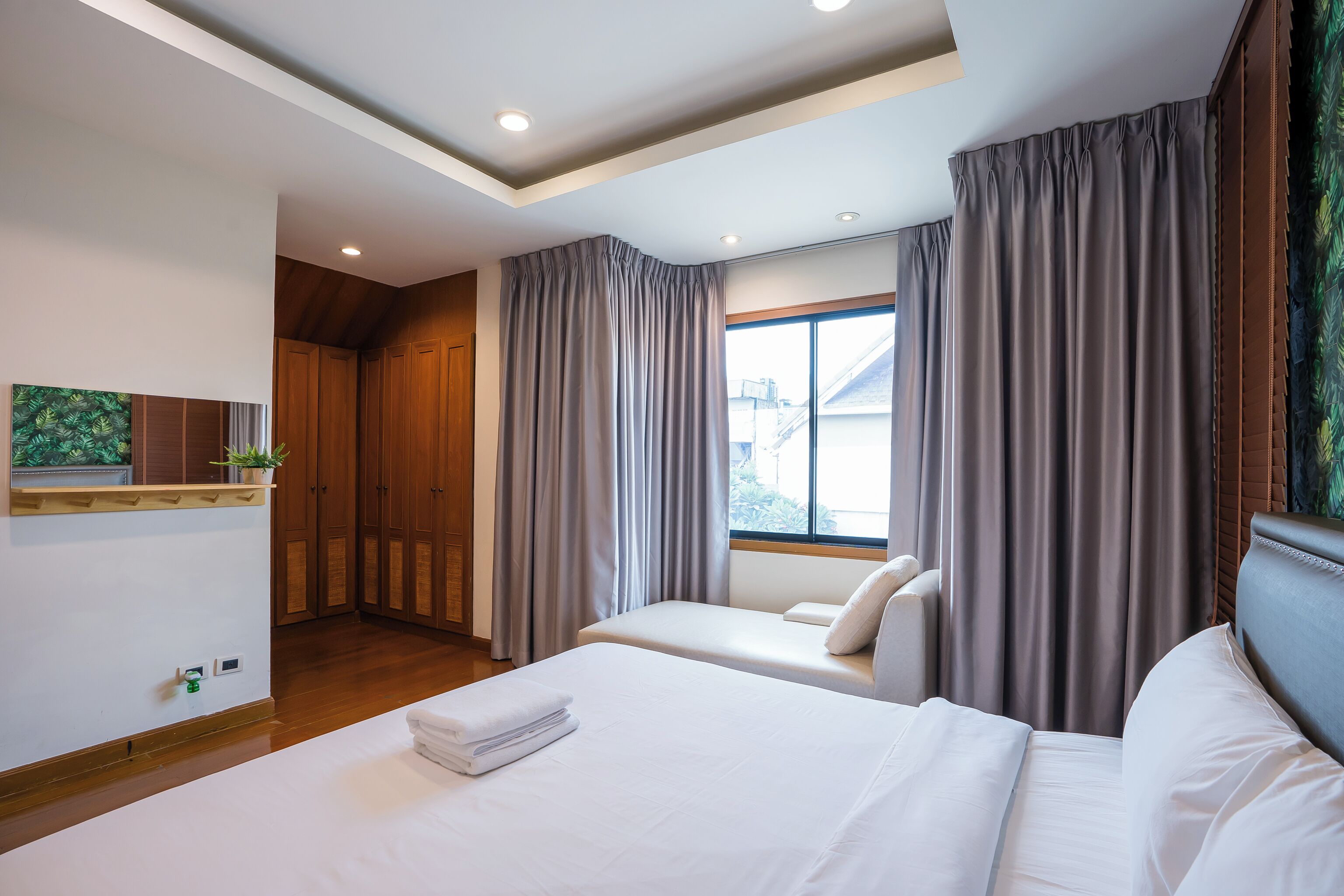 A hotel room with a large bed, a small sofa, wooden flooring, a window with curtains, and a ceiling with recessed lighting.