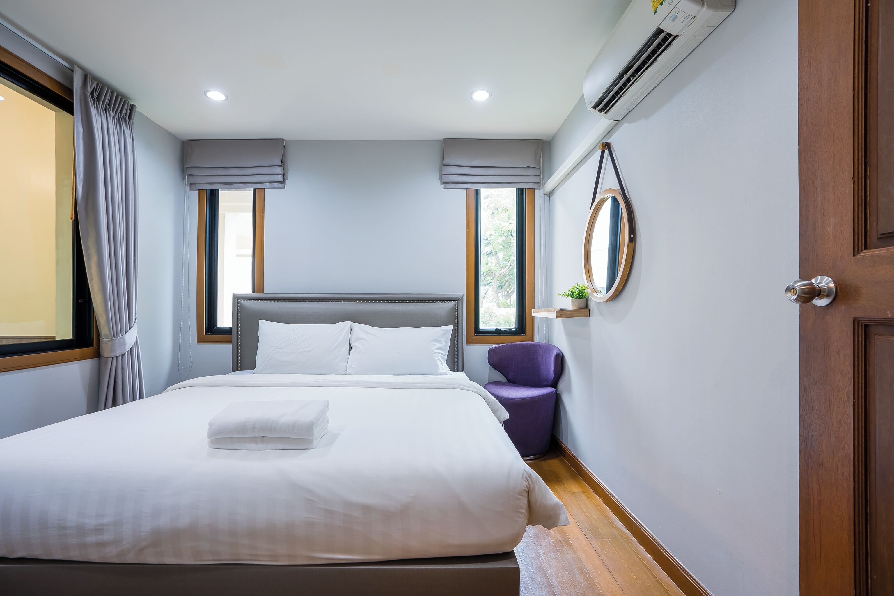 A neatly made bed with white linens, a grey headboard, and a small purple chair beside it.