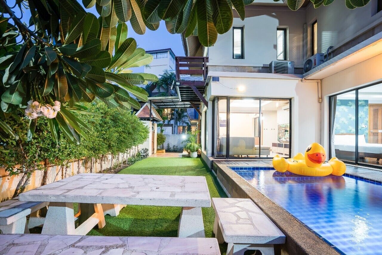 A modern outdoor pool area with a floating duck, a stone table, and a well-maintained lawn.