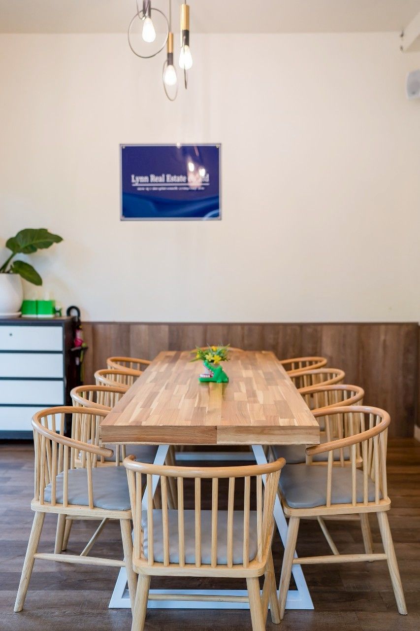 A dining area with a wooden table and six chairs, a potted plant, and a sign on the wall.