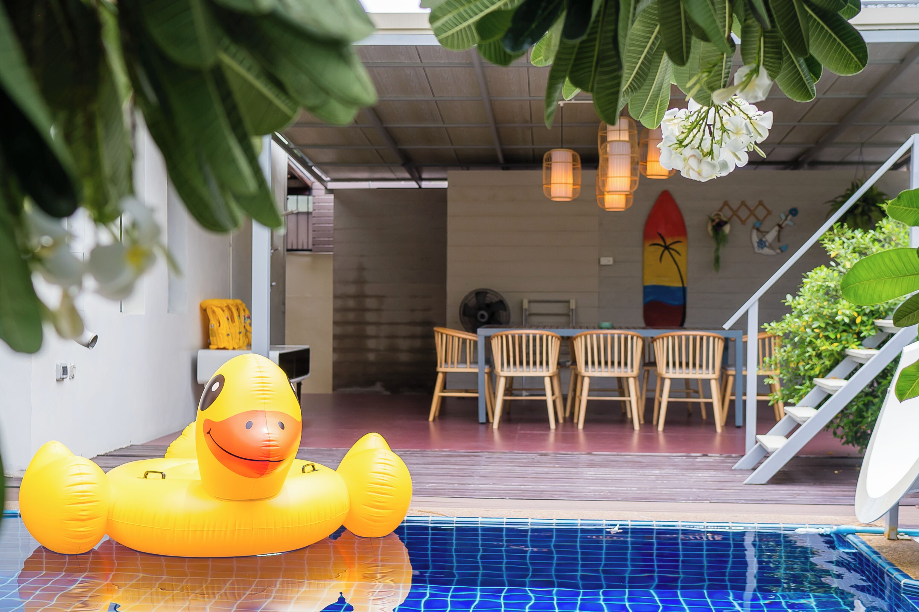 Una piscina interna con un'anatra gonfiabile gialla, sedie di legno e una tavola da surf appesa al muro.