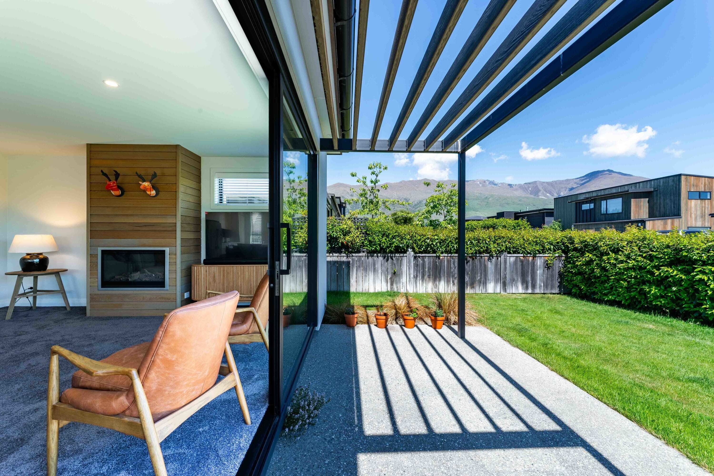 Un salon moderne avec une cheminée, un canapé et un téléviseur. Une porte vitrée donne sur un patio offrant une vue sur les montagnes.