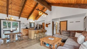 Een ruime woonkamer met een houten plafond, een grote bank, een salontafel en een keuken met een bar.
