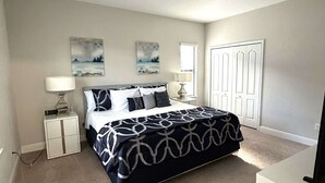A bedroom with a bed, two bedside tables, a nightstand, a window, and a door. - Contemporary pool home, gated community, resort facilities! (Haines City)