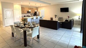 A modern living room with a dining area, a kitchen, and a TV mounted on the wall. - Contemporary pool home, gated community, resort facilities! (Haines City)