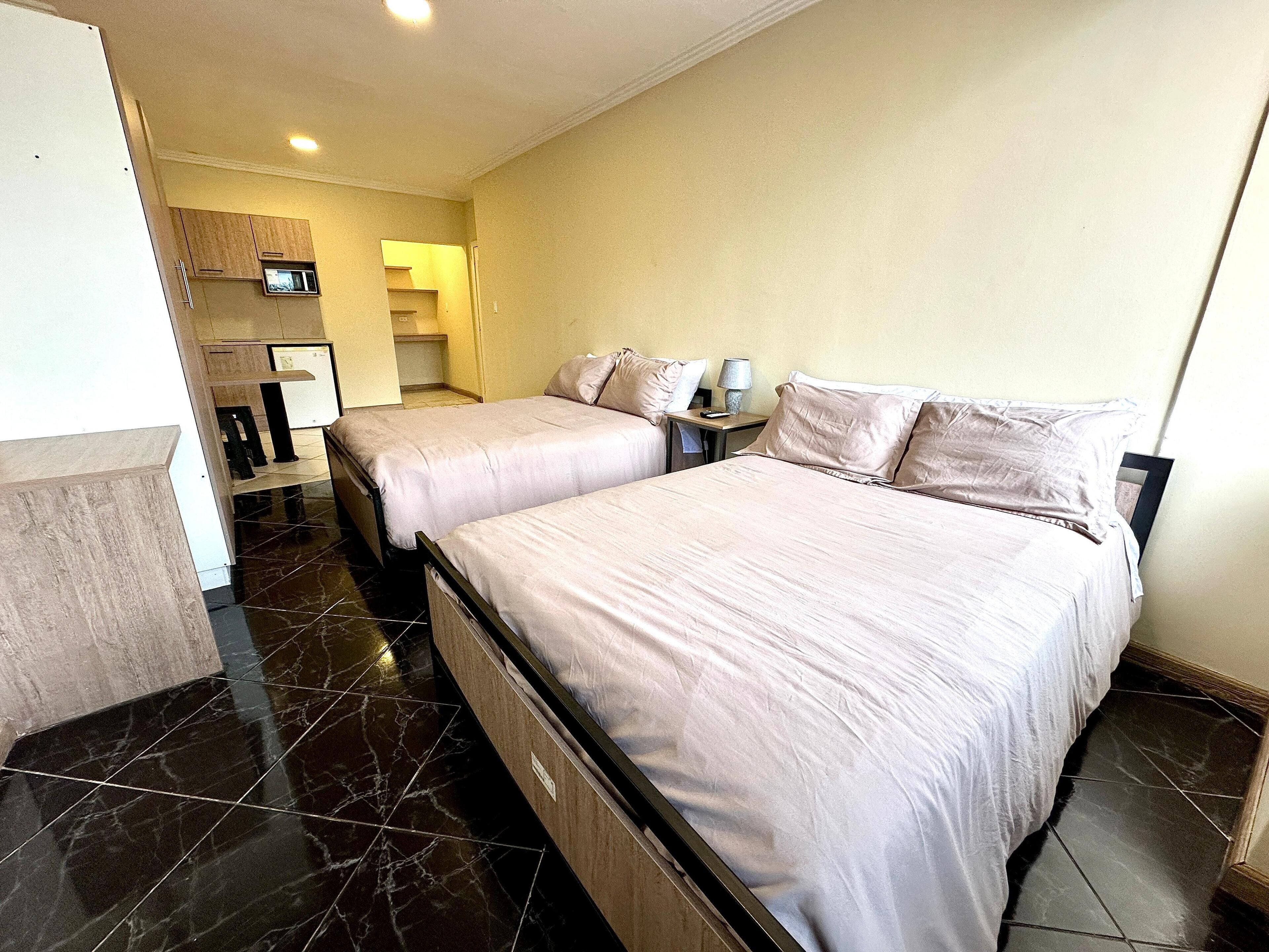 A hotel room with two beds, a small desk, a chair, a microwave, and a bathroom visible in the background.