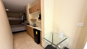 Une cuisine compacte équipée d’un lave-vaisselle intégré, une petite table à manger avec des tabourets et un lit à l’arrière-plan.