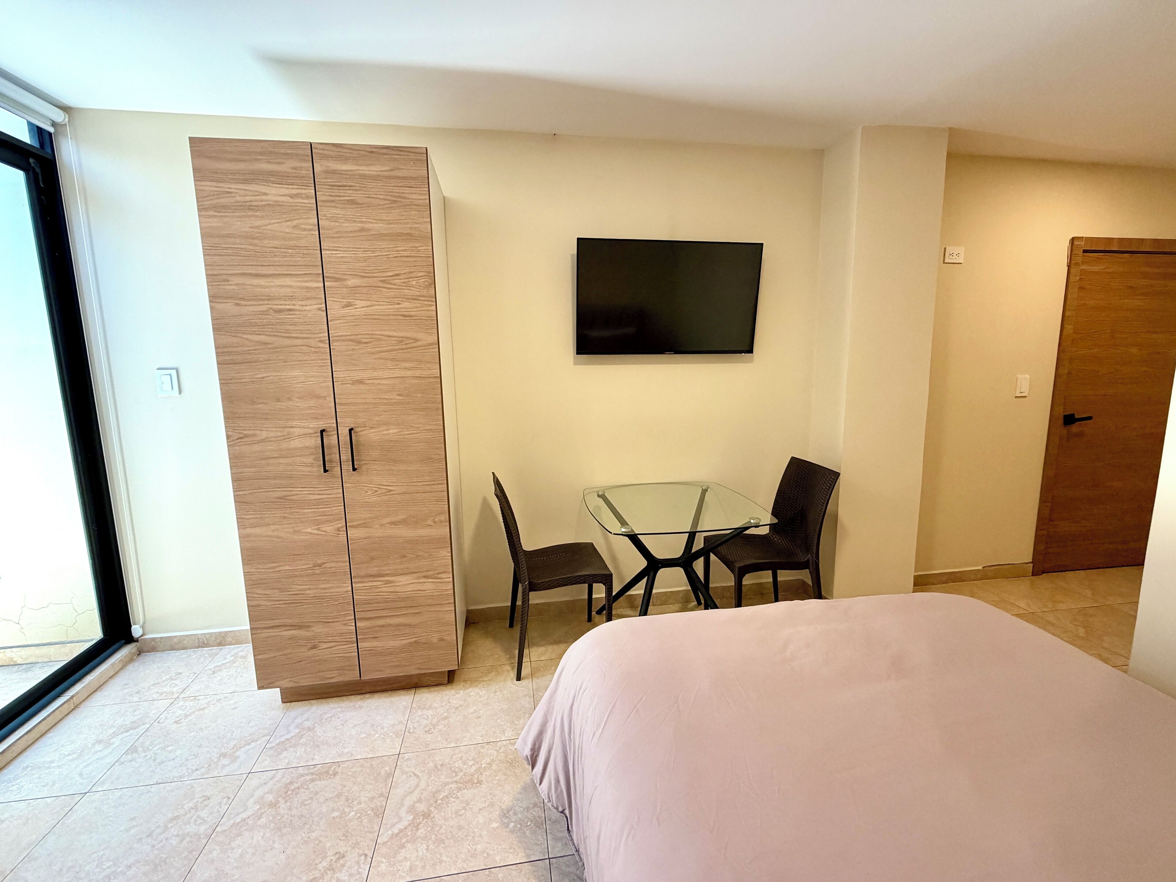 A bedroom with a bed, a wardrobe, a TV, and a small table with chairs.