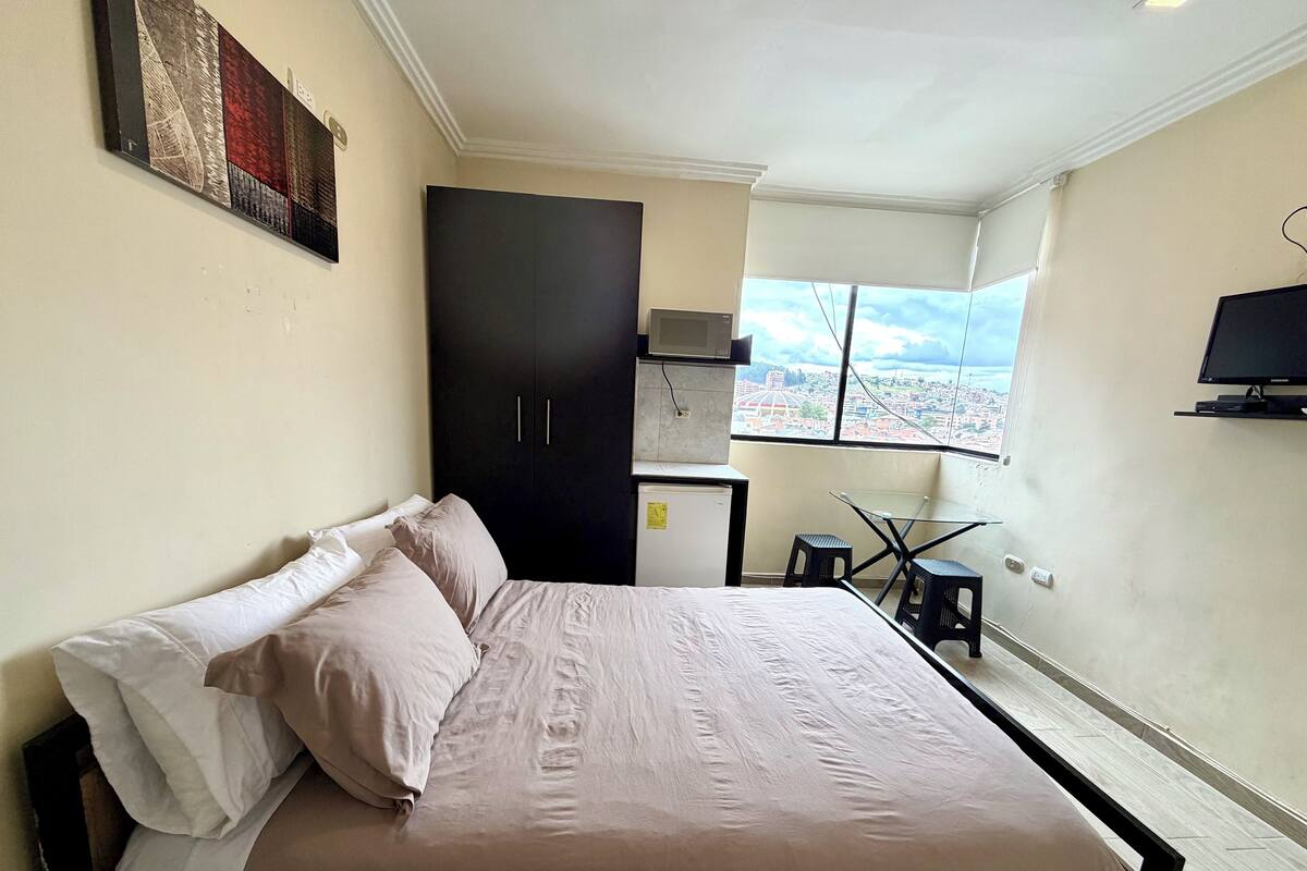A bedroom with a bed, a wardrobe, a small table, a chair, and a TV.