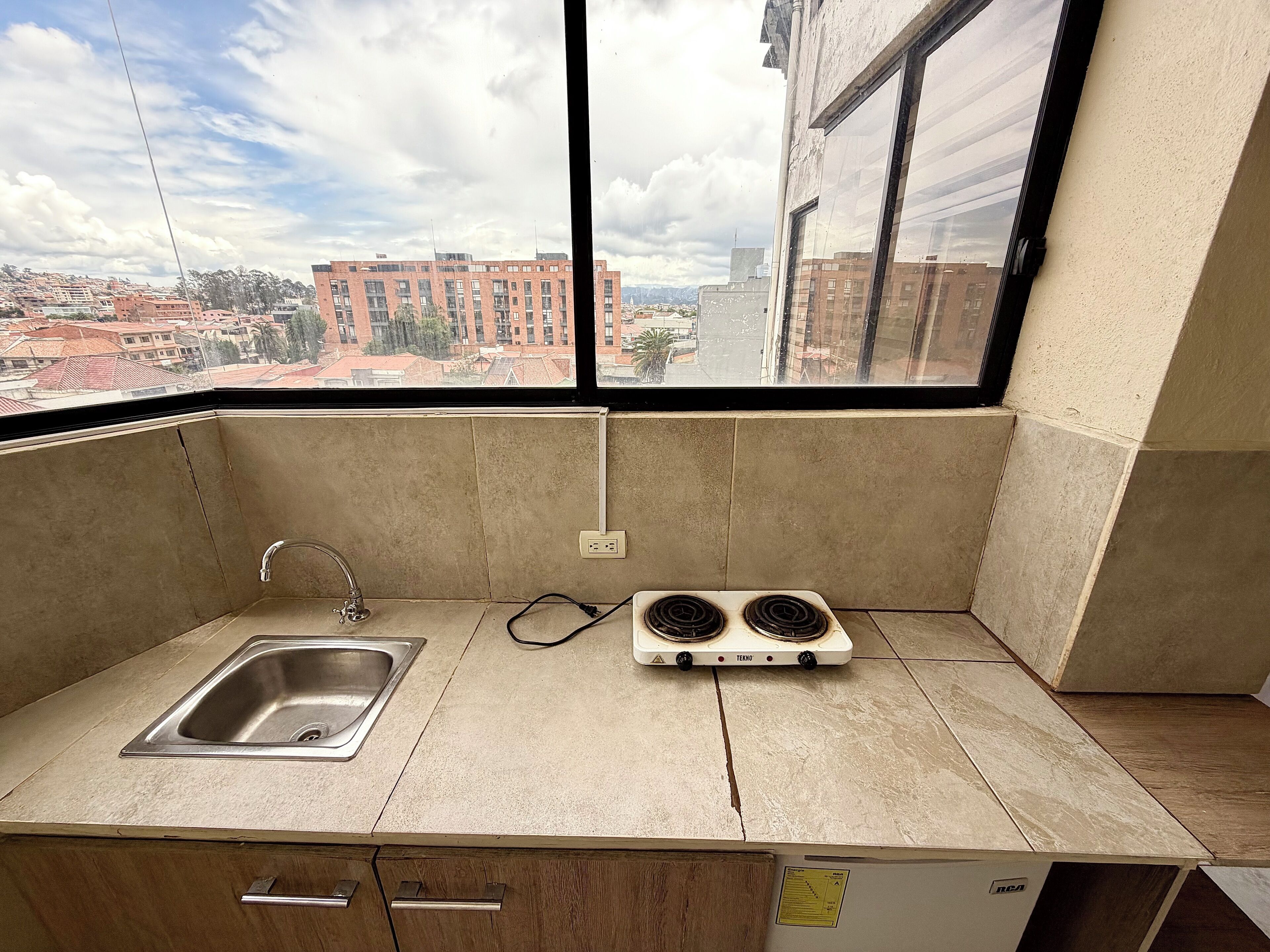 A small kitchenette with a sink, two burners, and a window overlooking a cityscape.