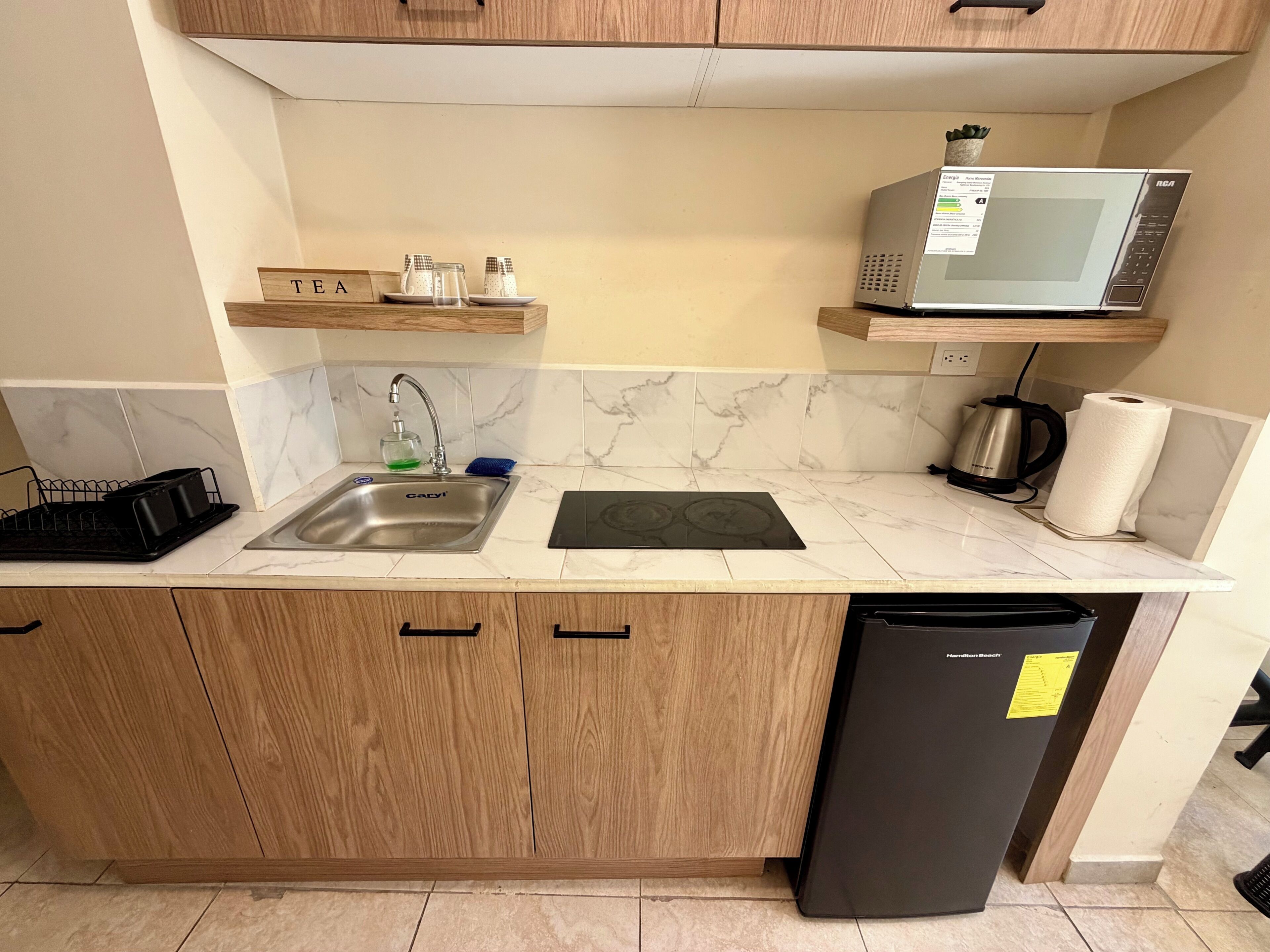 A kitchen with a sink, a microwave, a dish rack, and a refrigerator.