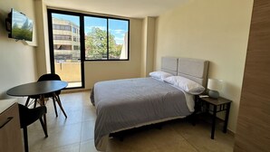 Une chambre d’hôtel équipée d’un lit, d’un bureau, d’une chaise, d’une télévision et offrant une vue sur l’extérieur.